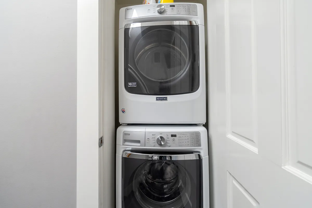 This practical space features a stacked washer and dryer with laundry supplies organized nearby, reflecting a functional corner often found in a mudroom or adjacent area. The setup is clean and efficient, ideal for families managing gear and clothing after outdoor adventures.