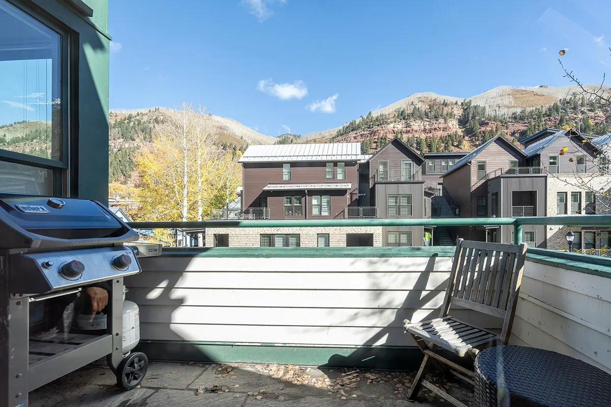 A deck with Adirondack chairs and a full-sized grill overlooks the mountains. The outdoor seating area is poised for both relaxing with a coffee at sunrise and grilling at sunset, with panoramic views enhancing the experience.