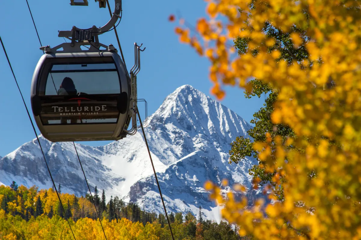 This image features the Telluride gondola gliding above a colorful autumn landscape with snow-capped mountains in the background. The gondola is a focal point, symbolizing easy access to ski slopes in winter and hiking/biking trails in summer. The vivid autumn foliage illustrates the area's year-round adventure potential.