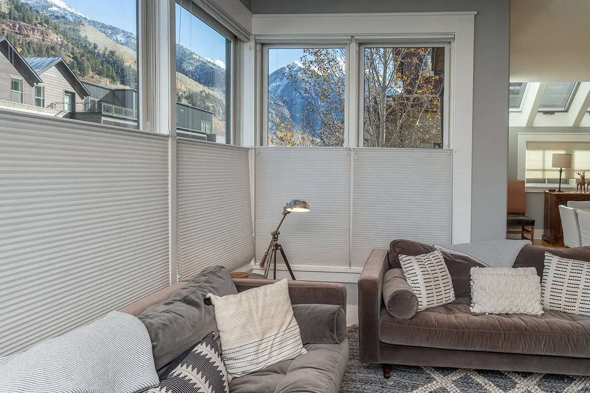 A comfortable seating area with plush chairs is arranged around a modern lamp. The space is defined by large windows that frame expansive mountain views, flooding the room with natural sunlight and providing a tranquil backdrop for relaxation or conversation.
