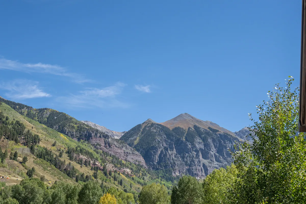 A panoramic view of majestic mountains under a clear blue sky, surrounded by lush greenery. The scene invites hiking, biking, and nature exploration, with an abundance of trails and vast wilderness.